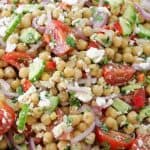 A vibrant chickpea salad in a bowl, featuring chickpeas, chopped tomatoes, cucumbers, red onions, bell peppers, crumbled feta cheese, and fresh herbs, all mixed together. The salad looks fresh and colorful, perfect for a healthy meal.