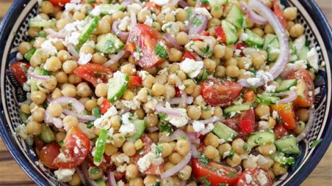 A vibrant chickpea salad in a bowl, featuring chickpeas, chopped tomatoes, cucumbers, red onions, bell peppers, crumbled feta cheese, and fresh herbs, all mixed together. The salad looks fresh and colorful, perfect for a healthy meal.