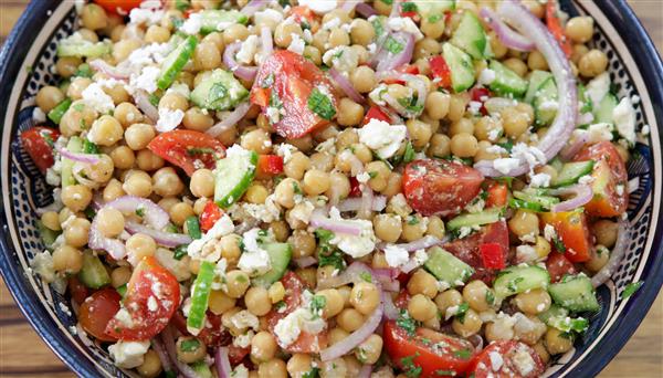 A vibrant chickpea salad in a bowl, featuring chickpeas, chopped tomatoes, cucumbers, red onions, bell peppers, crumbled feta cheese, and fresh herbs, all mixed together. The salad looks fresh and colorful, perfect for a healthy meal.