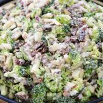 A bowl filled with a broccoli salad, featuring chopped broccoli, red onions, raisins, and nuts, all mixed with a creamy dressing. The salad appears fresh and colorful, with the green of the broccoli dominating the dish.