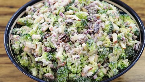 A bowl filled with a broccoli salad, featuring chopped broccoli, red onions, raisins, and nuts, all mixed with a creamy dressing. The salad appears fresh and colorful, with the green of the broccoli dominating the dish.