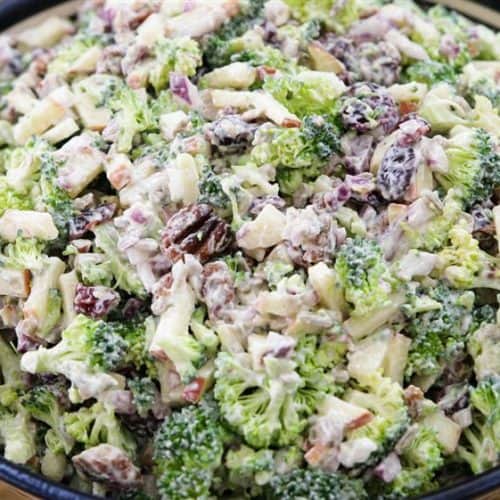 A bowl filled with a broccoli salad, featuring chopped broccoli, red onions, raisins, and nuts, all mixed with a creamy dressing. The salad appears fresh and colorful, with the green of the broccoli dominating the dish.