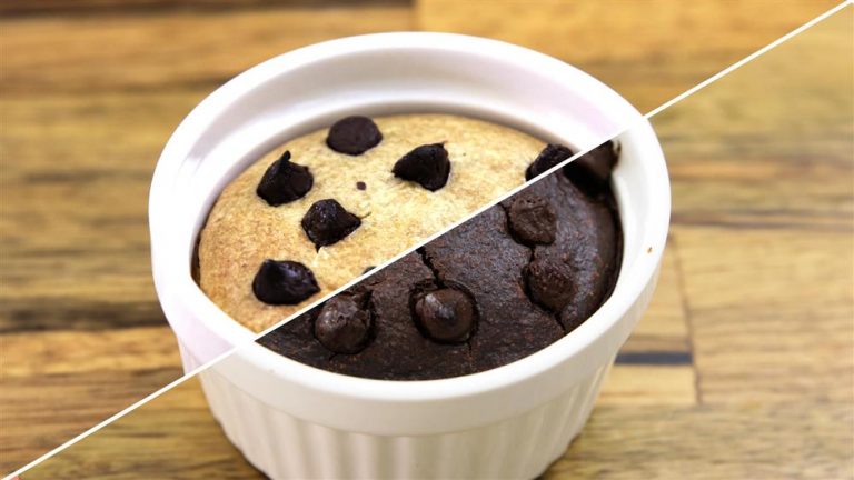 A white ceramic ramekin holds a half-and-half baked dessert, divided diagonally. The left half is a vanilla cake topped with chocolate chips, and the right half is a chocolate cake also topped with chocolate chips. The background is a wooden surface.