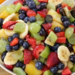 A vibrant bowl of fruit salad containing a mix of colorful fruits such as strawberries, blueberries, pineapple, kiwi, grapes, mango, and banana slices. The fruits are fresh and juicy, creating a visually appealing and appetizing dish.