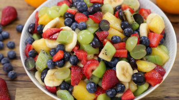 A vibrant bowl of fruit salad containing a mix of colorful fruits such as strawberries, blueberries, pineapple, kiwi, grapes, mango, and banana slices. The fruits are fresh and juicy, creating a visually appealing and appetizing dish.