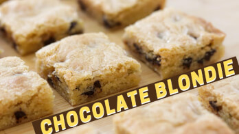 Close-up image of sliced chocolate blondies arranged on a wooden surface. The blondies have a golden-brown crust with visible chocolate chips. Text overlay at the bottom reads "CHOCOLATE BLONDIE.