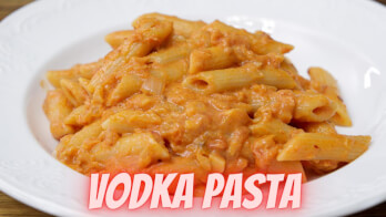 A white plate filled with penne pasta in a creamy tomato vodka sauce. The text "VODKA PASTA" is prominently displayed at the bottom of the image in bold, pink letters.