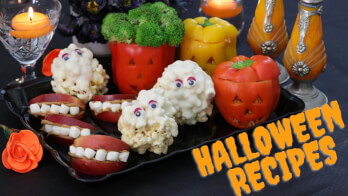 A platter of Halloween-themed snacks, including apple slices with marshmallows resembling monster mouths, popcorn balls with candy eyes, and bell peppers carved like jack-o'-lanterns filled with broccoli. The text "HALLOWEEN RECIPES" is displayed in the bottom right corner.