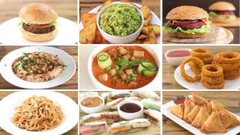 A collage of nine vegan dishes on a wooden table. Includes a veggie burger, guacamole with chips, a beet burger, hummus, zucchini soup, onion rings, noodle stir-fry, spring rolls with dipping sauces, and samosas with chutneys.