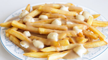 A plate of poutine, featuring golden French fries topped with cheese curds and smothered in light brown gravy, is shown on a white plate with blue decorative trim.