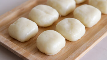 A wooden tray holds nine evenly spaced, plump, white steamed buns. The smooth, shiny surface of each bun suggests they are freshly prepared and soft.