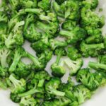 A white skillet filled with vibrant green broccoli florets, lightly sautéed. The skillet is on a wooden surface.