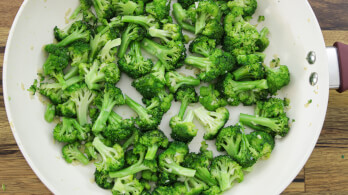 A white skillet filled with vibrant green broccoli florets, lightly sautéed. The skillet is on a wooden surface.