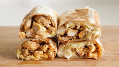 Four halves of grilled chicken wraps filled with juicy chicken, melted cheese, and sauce, neatly stacked on a wooden surface. The wraps are toasted golden brown and slightly crispy on the outside.