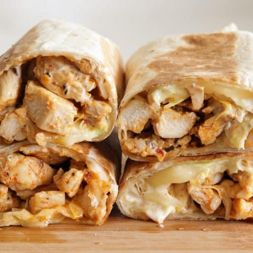 Four halves of grilled chicken wraps filled with juicy chicken, melted cheese, and sauce, neatly stacked on a wooden surface. The wraps are toasted golden brown and slightly crispy on the outside.