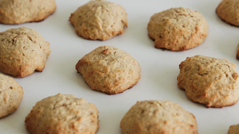 A close-up view of freshly baked cookies arranged in neat rows on parchment paper. The cookies are golden brown, slightly cracked on the top, and appear soft and fluffy.