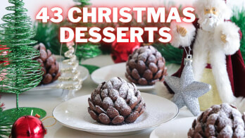 A festive scene featuring multiple plates of Christmas desserts resembling pinecones, dusted with powdered sugar. The background includes green decorative Christmas trees, ornaments, and a Santa Claus figure. Text at the top reads "43 Christmas Desserts.