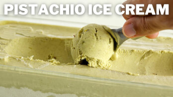 A hand is shown scooping pistachio ice cream from a rectangular container. The text "PISTACHIO ICE CREAM" is displayed at the top of the image. The ice cream has a creamy, light green color typical of pistachio flavor.