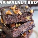 Three banana walnut brownies are stacked on a white plate. They are rich and dark in color, with visible walnut pieces embedded throughout. The text "BANANA WALNUT BROWNIES" is displayed at the top of the image. A cooling rack with more brownies is in the background.