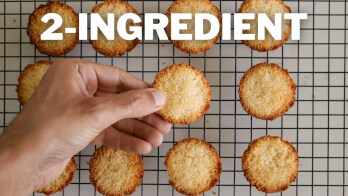 A hand is picking up one of several golden-brown baked goods from a cooling rack. Bold white text at the top reads "2-INGREDIENT.