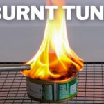 A can of tuna sits on a wire rack with intense flames shooting out from its top. The words "BURNT TUNA" are displayed prominently above the image.