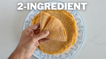 A hand is holding a folded piece of a flat, round food item on a blue and white floral plate. The text "2-INGREDIENT" is prominently displayed at the top of the image.