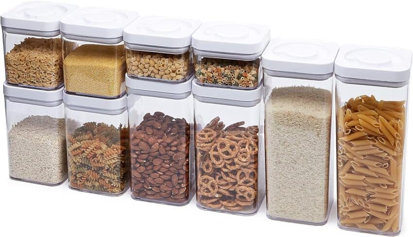 A set of ten clear rectangular containers with white lids, filled with various dry goods including pasta, beans, rice, pretzels, and grains, neatly organized in a row.