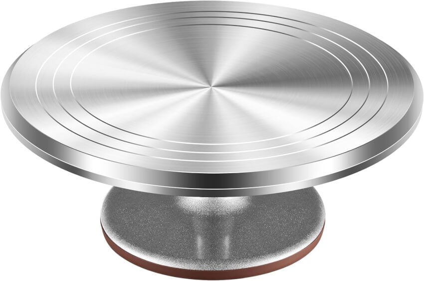 A stainless steel rotating cake turntable with a circular design on the surface, sitting on a round, sturdy base. The turntable appears to be designed for decorating cakes with precision, providing smooth rotation for easy access from all angles.