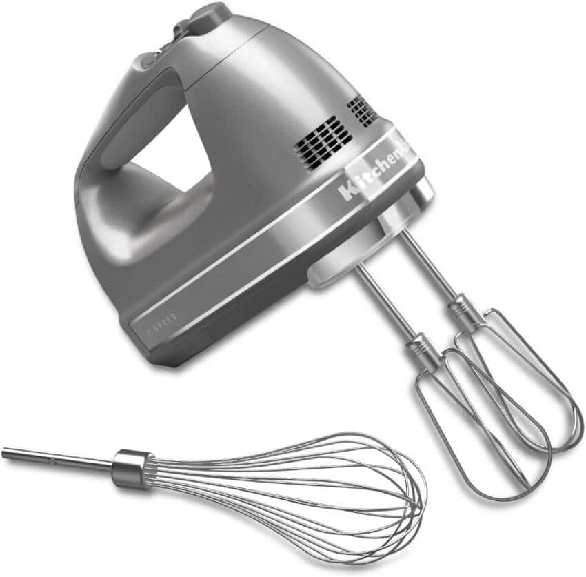 A sleek, silver KitchenAid hand mixer with two attached beaters and an additional whisk attachment placed beside it. The mixer has a comfortable handle and a modern design, suitable for various mixing tasks in the kitchen.