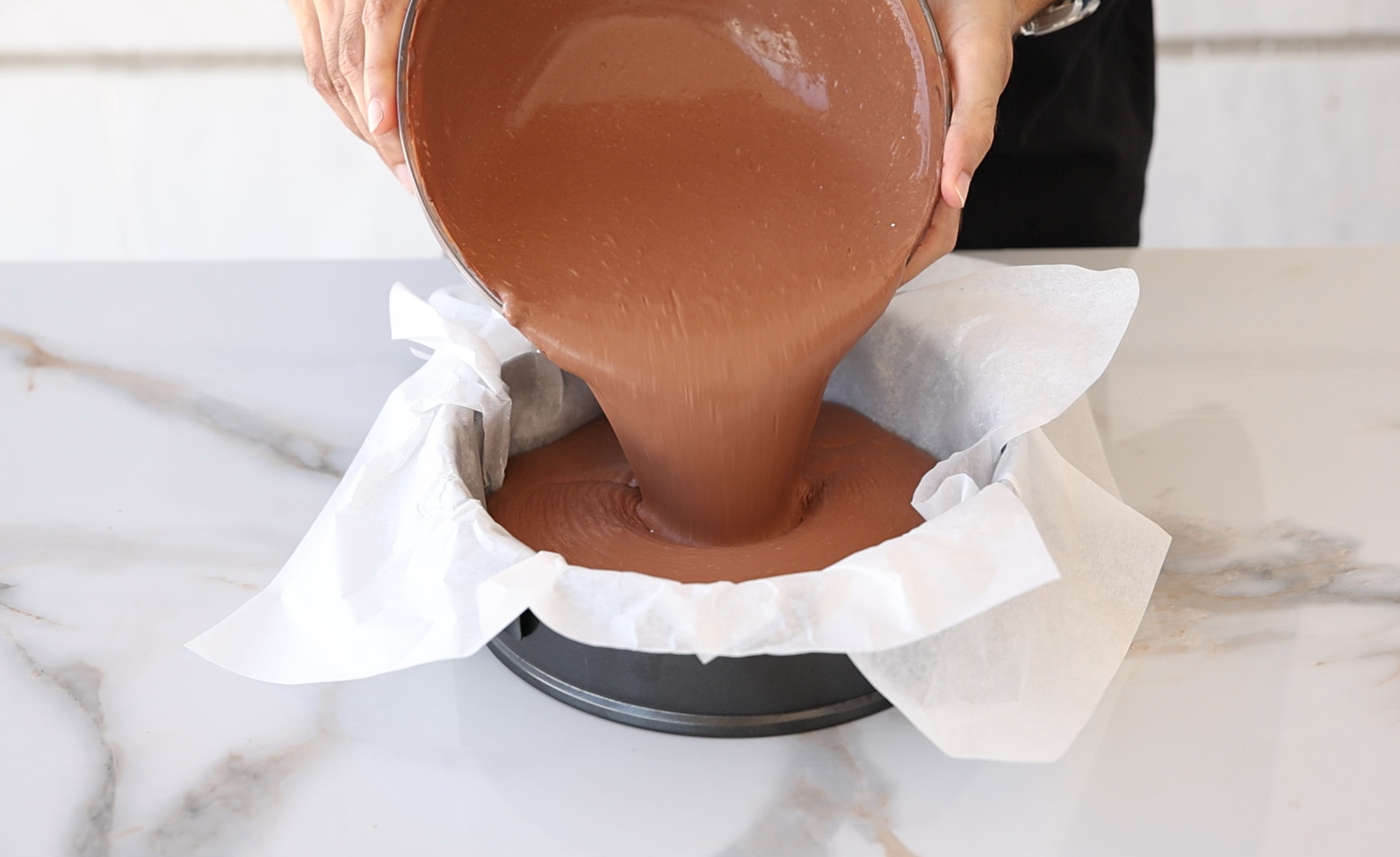 pouring chocolate cheesecake batter into a pan