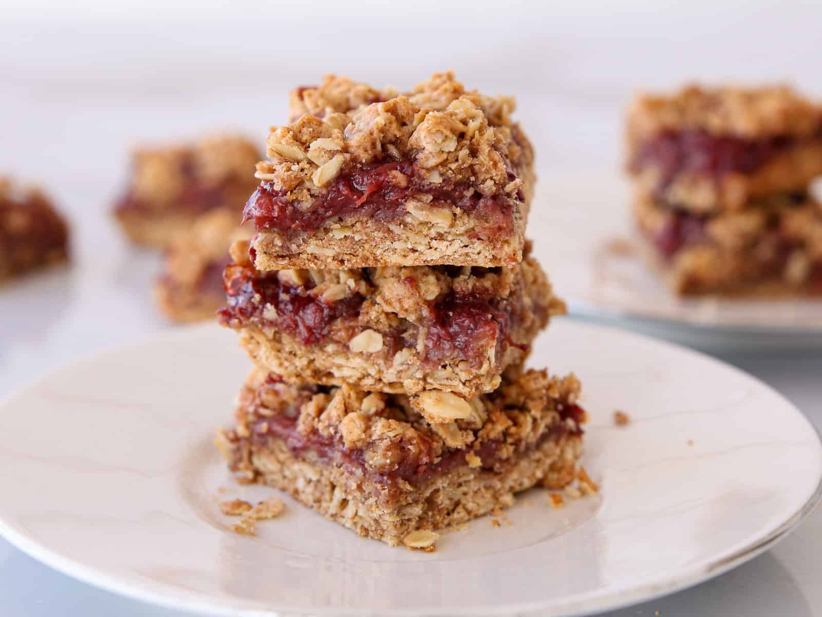 Three oat and jam bars stacked on a plate. 