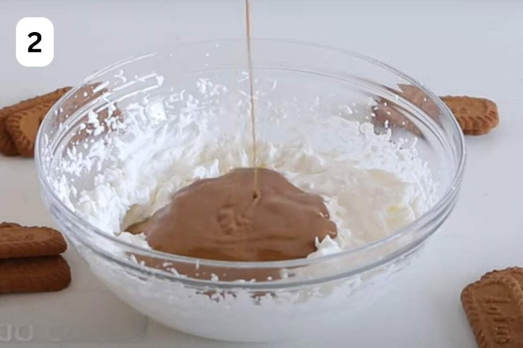 pouring melted biscoff cream in the whipped cream.