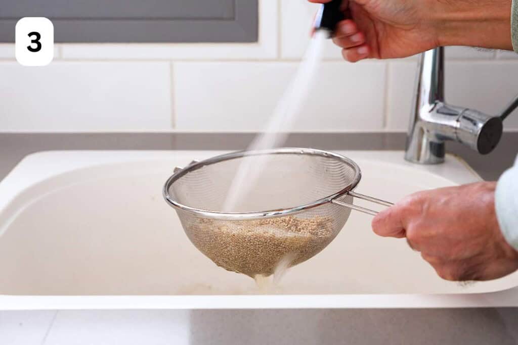 rinsing quinoa in a mesh strainer under water.