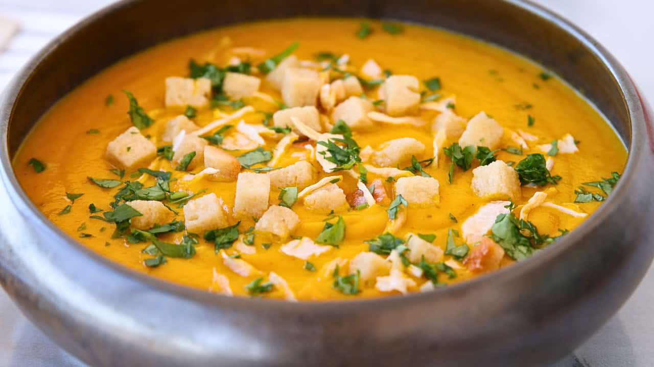 a bowl of carrot and ginger soup topped with croutons and chopped parsley