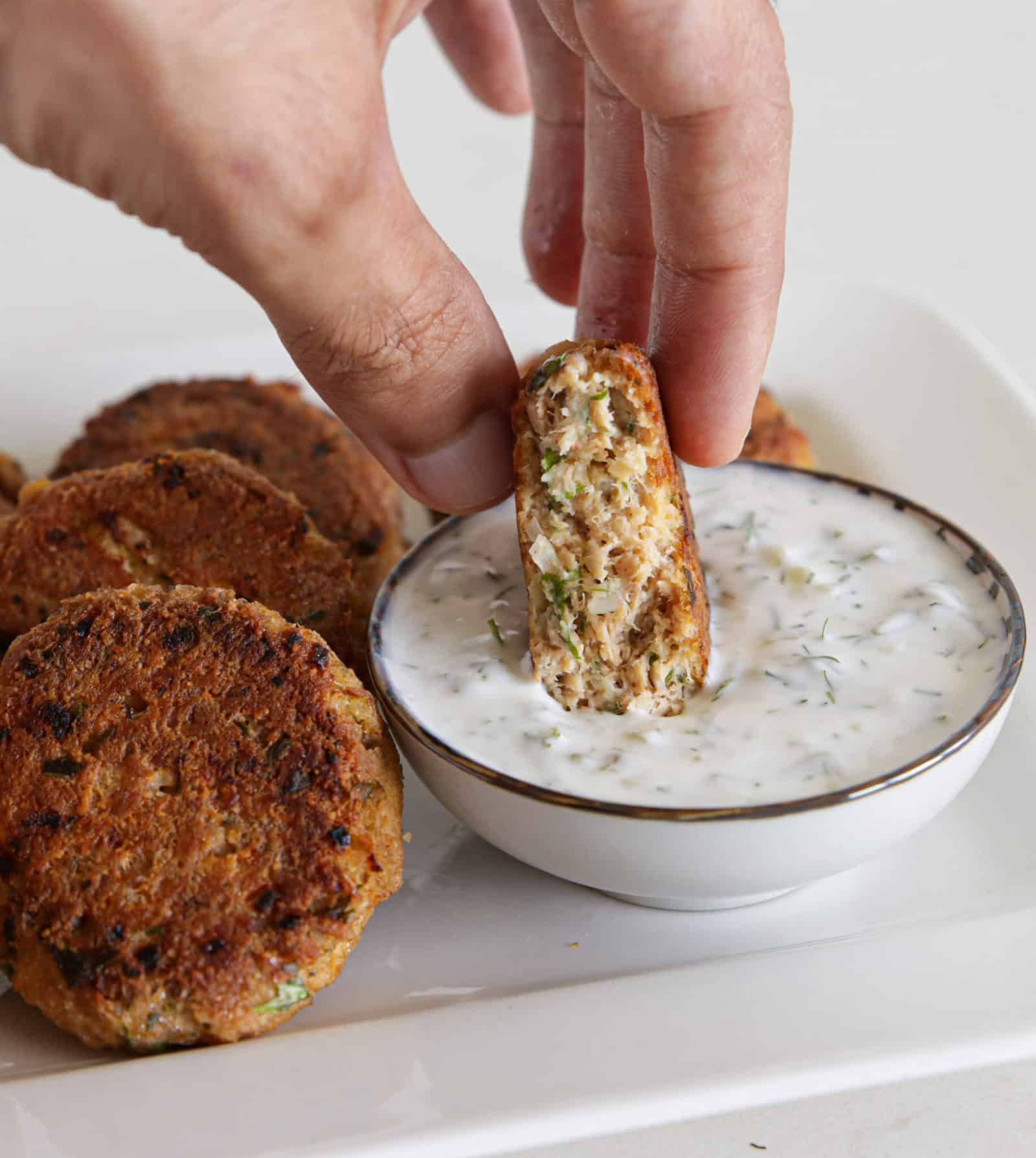 hand dipping a tuna patty into dipping sauce.