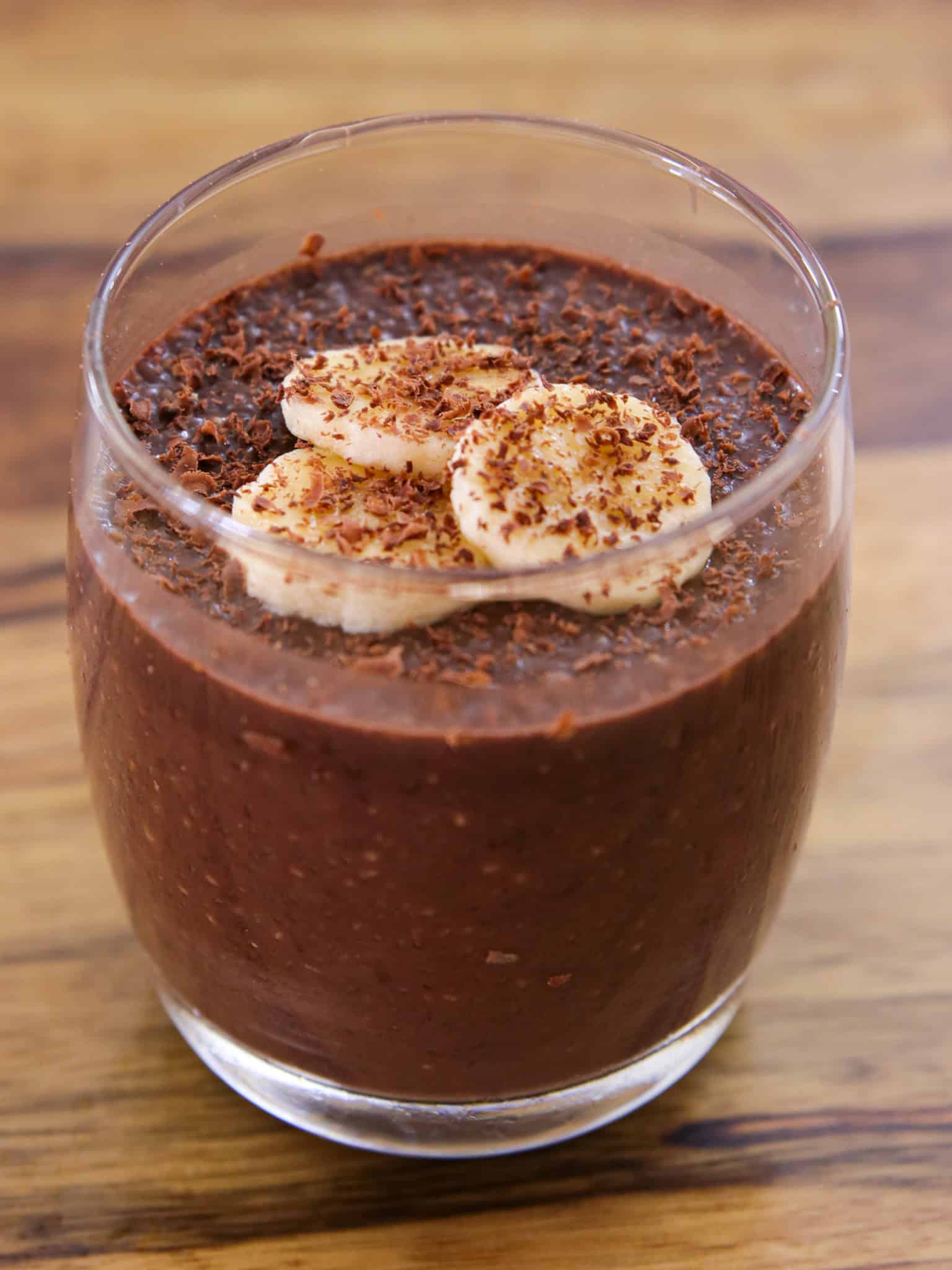 chocolate banana chia pudding in a glass with banana slices on top and chocolate shavings