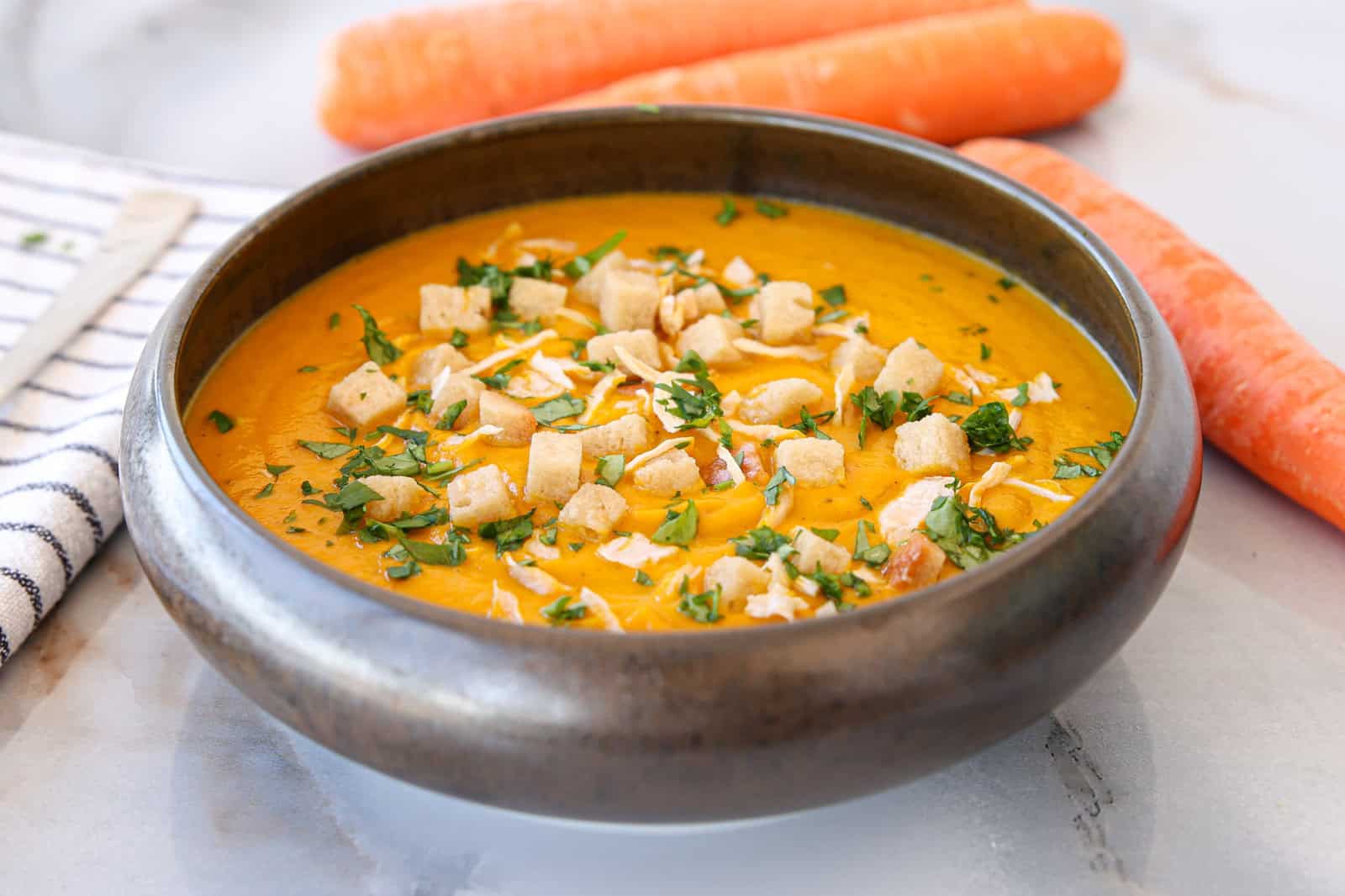 a bowl of carrot and ginger soup served with croutons, caramelized onions and parsley 