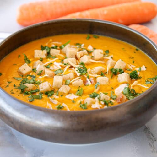 a bowl of creamy carrot and ginger soup with fresh carrot in the background