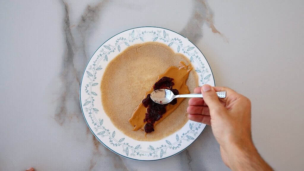 spoon spreading peanut butter and jelly on a crepe.