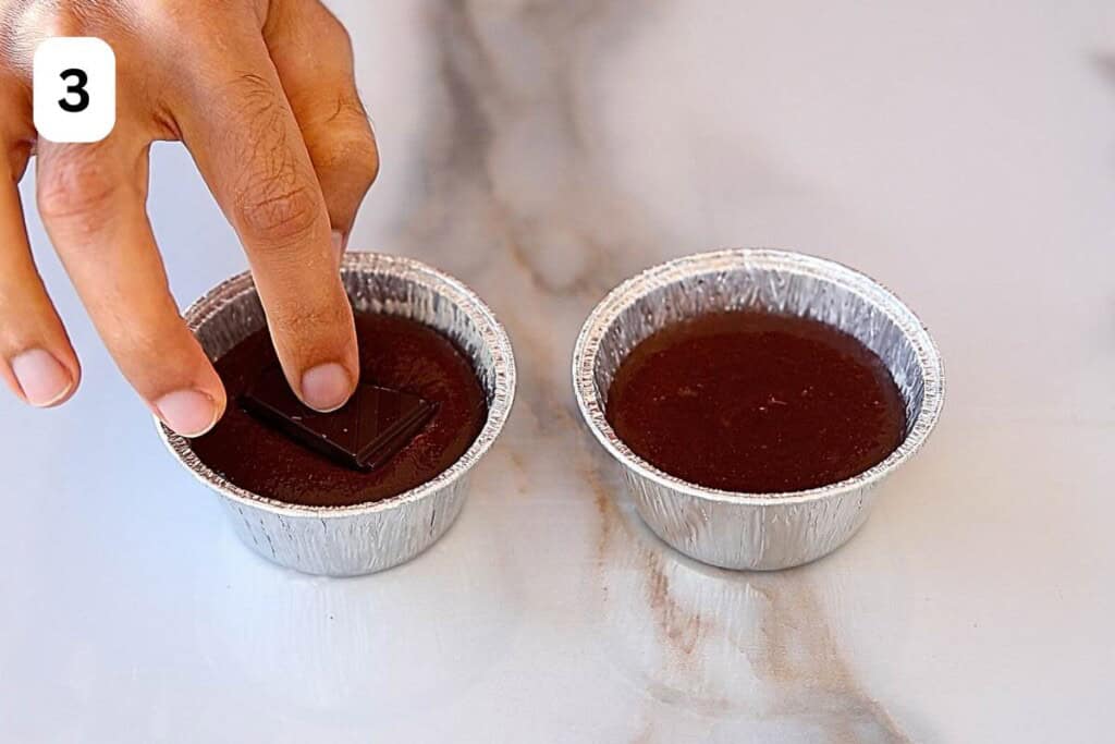 hand adding a chocolate square into the raw lava cakes.