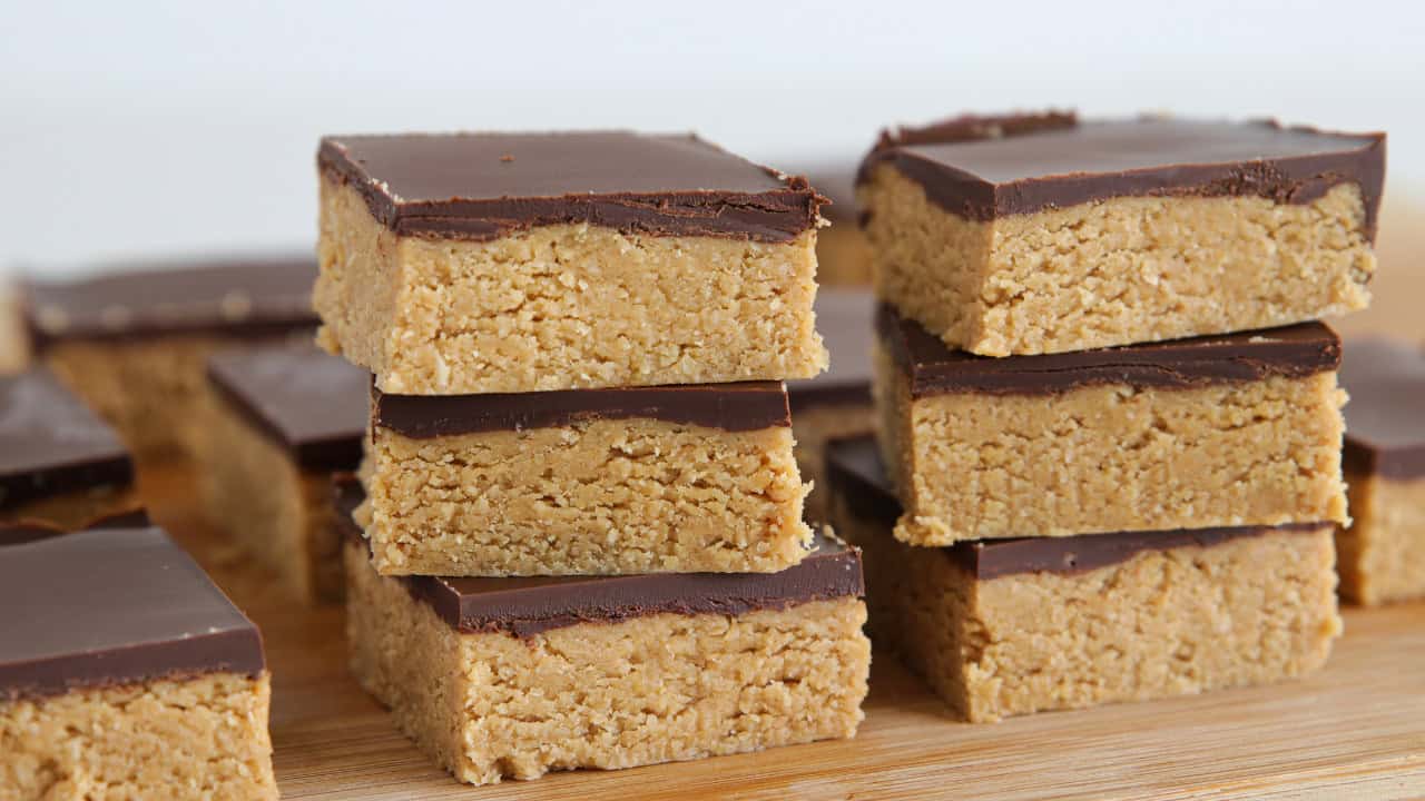 Close-up of multiple bars of chocolate-topped peanut butter fudge squares arranged in rows on a cooling rack. The bars have a thick layer of chocolate on top and a dense, golden-brown peanut butter layer underneath.