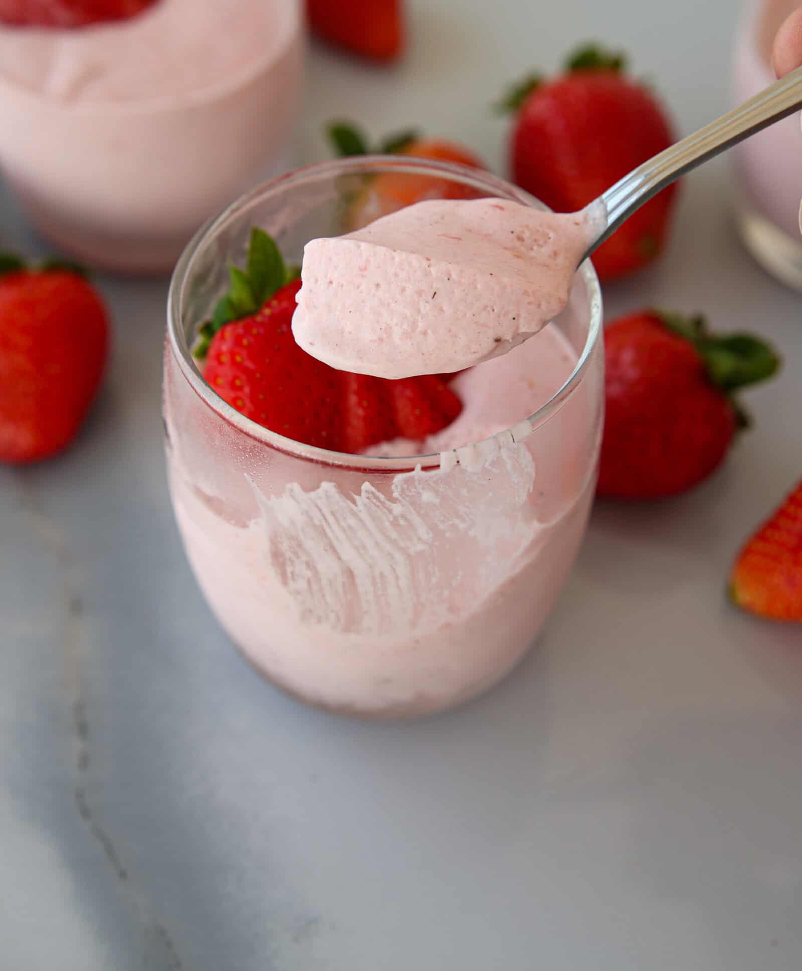 a teaspoon holding a ping strawberry mousse above a glass filled with mouse and fresh strawberries