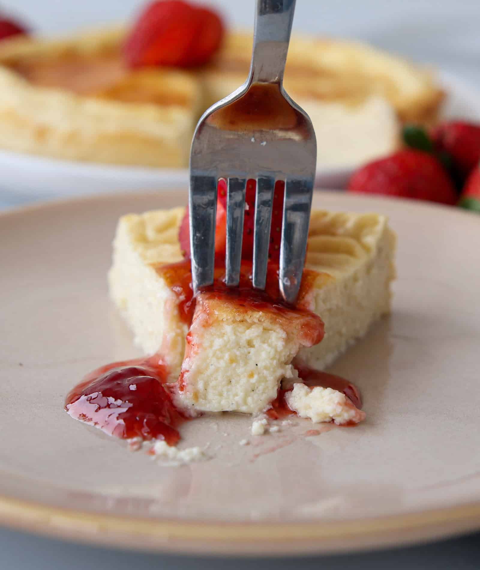 a fork goes into a slice of a creamy cheesecake topped with jam