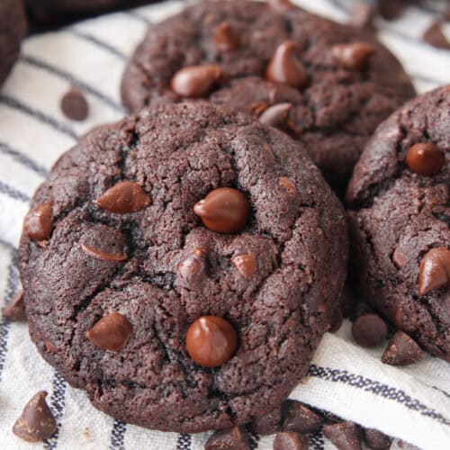 a batch of Double chocolate chip cookies on a white towel with chocolate chips in the background