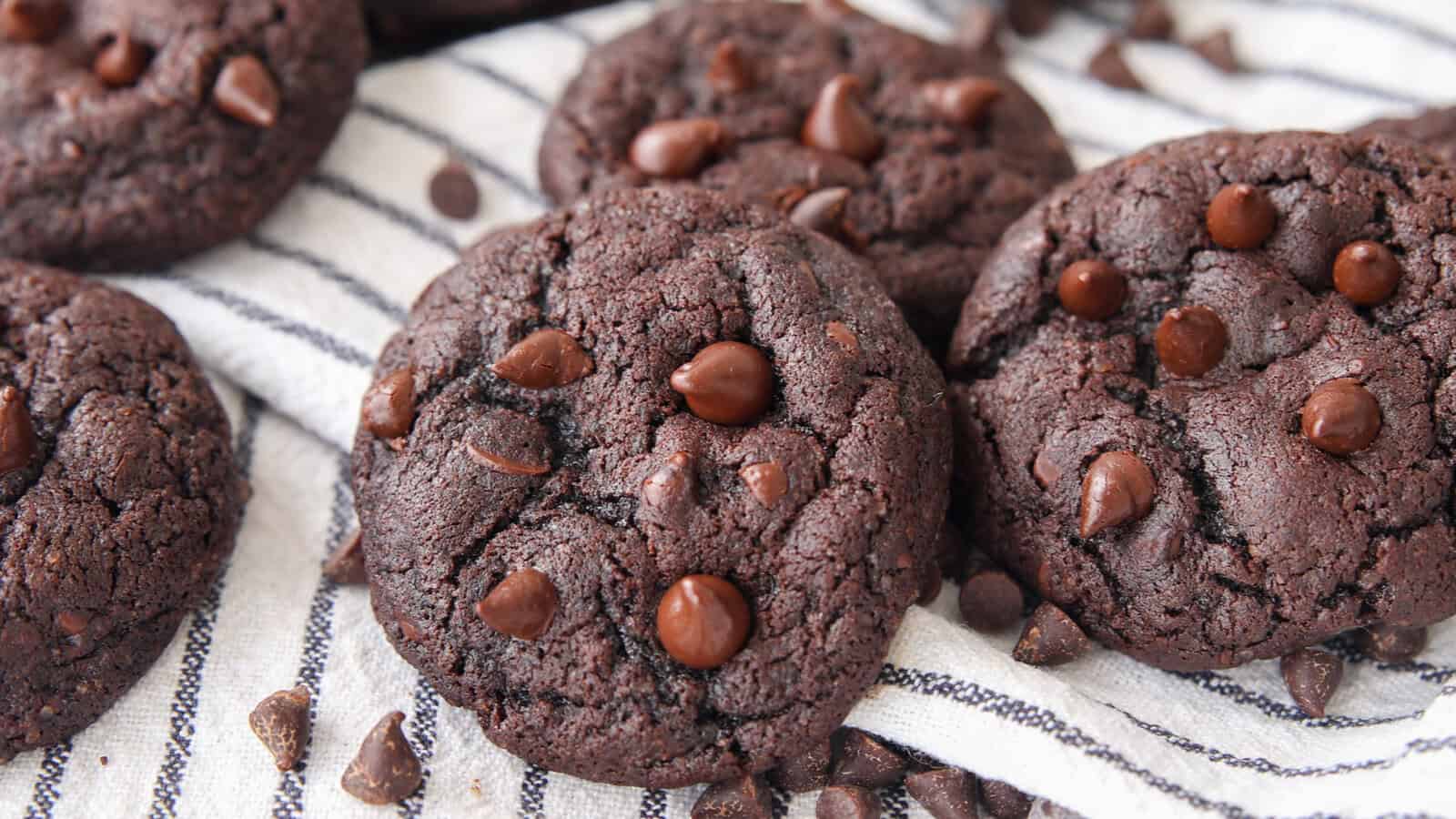 a batch of Double chocolate chip cookies on a white towel with chocolate chips in the background