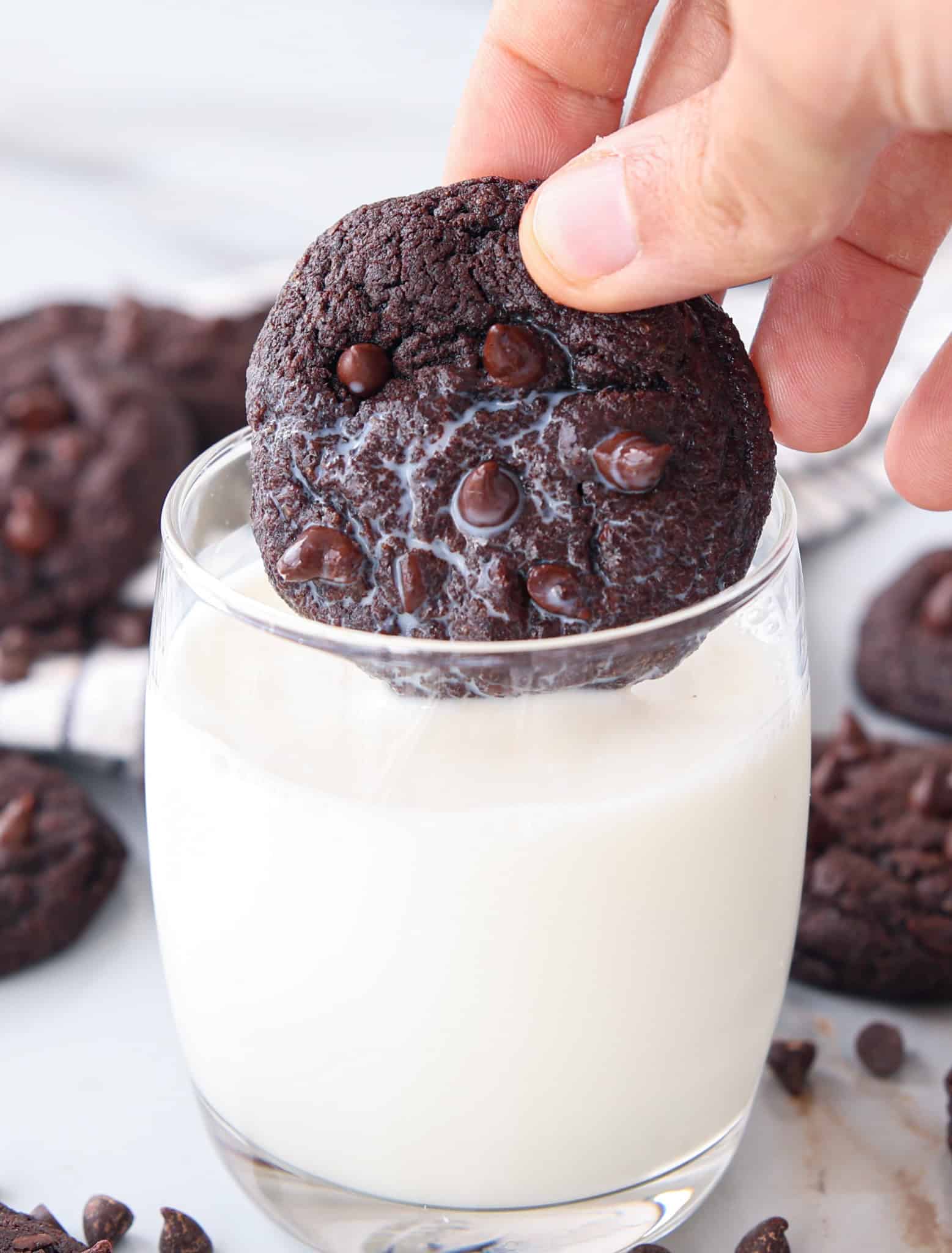 a hand holding and dipping a chocolate cookie into a glass of milk