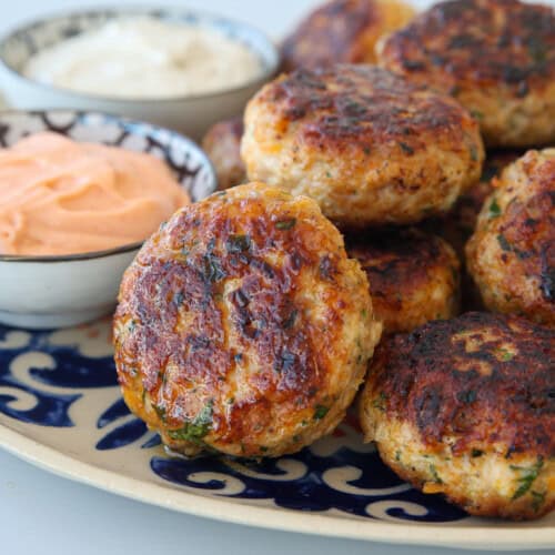 a batch of crispy and juicy chicken patties on a plate along side with two dipping sauces