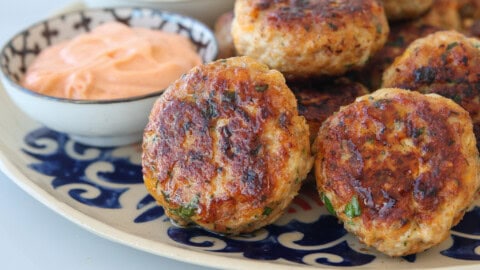 a batch of crispy and tender chicken patties on a large plate, in the background there are two dippings, spicy mayo and tahini yogurtsauce