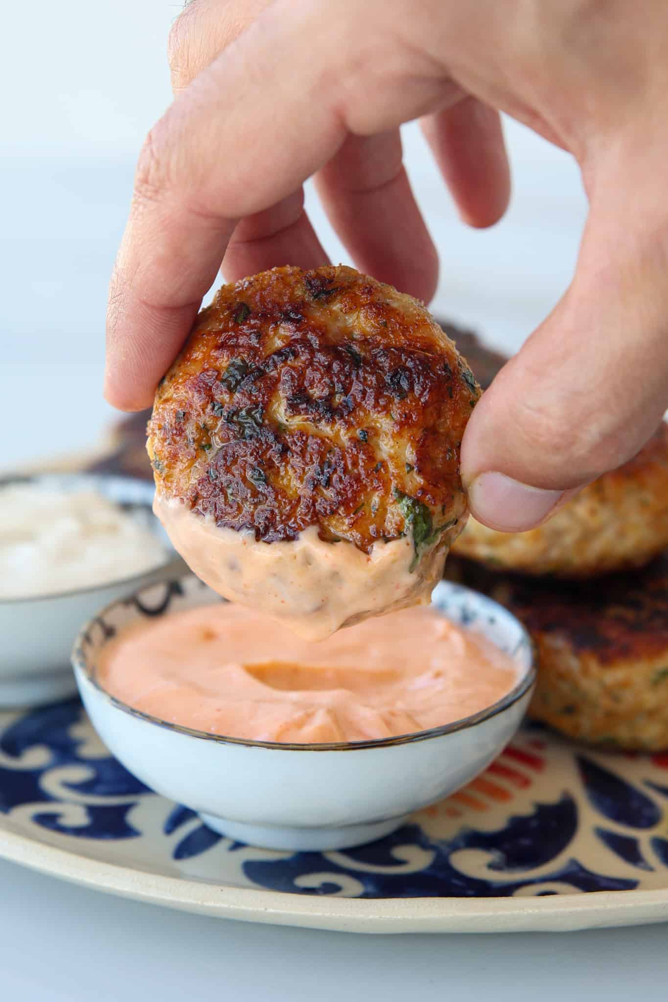 a hand holding a juicy chicken patty that eas dipping in a spicy mayo dipping sauce