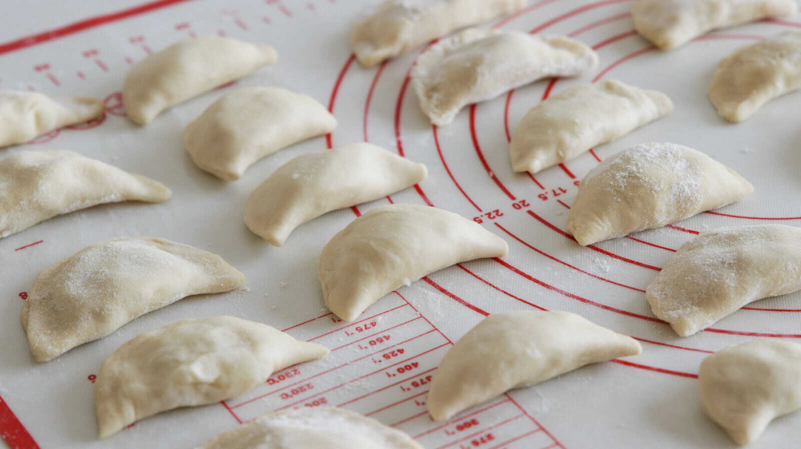 a bunch of uncooked pierogis on a baking mat